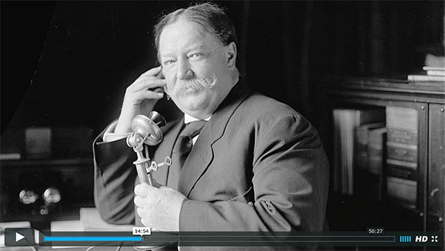 A screenshot from a video of Howard Taft talking on the telephone