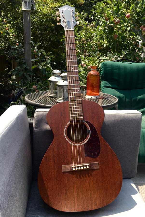 The guitar seated on porch furniture.